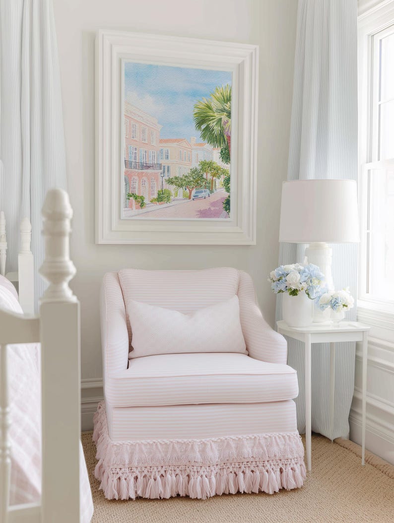 May include: A light pink striped armchair with a matching fringed skirt and a white pillow. A framed watercolor painting of a street scene hangs above the chair. A white side table holds a lamp and flowers.