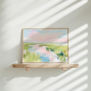 Op de afbeelding: Een rechthoekig landschapsschilderij in een lichthouten lijst met een moeraslandschap met zachte penseelstreken van roze, lichtblauw en diverse tinten groen. Het kunstwerk toont een kronkelende waterweg die de lucht boven het grasland weerspiegelt.