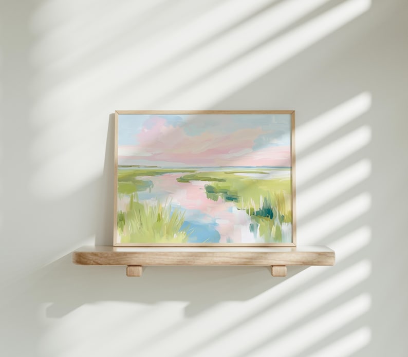 Op de afbeelding: Een rechthoekig landschapsschilderij in een lichthouten lijst met een moeraslandschap met zachte penseelstreken van roze, lichtblauw en diverse tinten groen. Het kunstwerk toont een kronkelende waterweg die de lucht boven het grasland weerspiegelt.