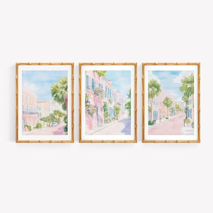 May include: A set of three framed watercolor prints depicting street scenes with pink buildings, green palm trees, and blue skies. Each print is enclosed in a gold-toned bamboo-style frame, showcasing architectural details and lush foliage.