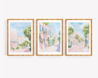 May include: A set of three framed watercolor prints depicting street scenes with pink buildings, green palm trees, and blue skies. Each print is enclosed in a gold-toned bamboo-style frame, showcasing architectural details and lush foliage.