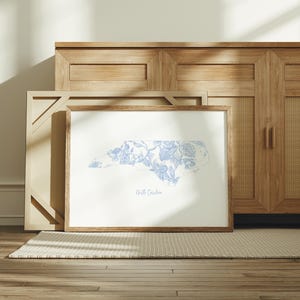 May include: A framed print of the state of North Carolina with a blue and white floral pattern. The print is on a white background and has the words "North Carolina" printed below the state outline.