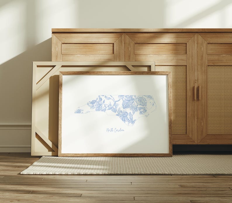 May include: A framed print of the state of North Carolina with a blue and white floral pattern. The print is on a white background and has the words "North Carolina" printed below the state outline.