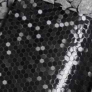 May include: A close-up of a black fabric with a repeating honeycomb pattern. The pattern is made up of small, six-sided shapes in varying shades of black and gray, creating a textured appearance. Some of the shapes have a reflective, shiny quality.
