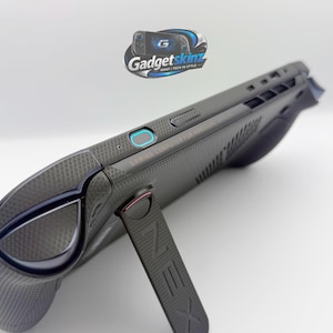 May include: A handheld gaming computer featuring a dark grey textured skin with a hexagonal pattern. The device includes a built-in kickstand with the letter Z embossed on it, a power button with a blue light ring, and various ports along the top edge.