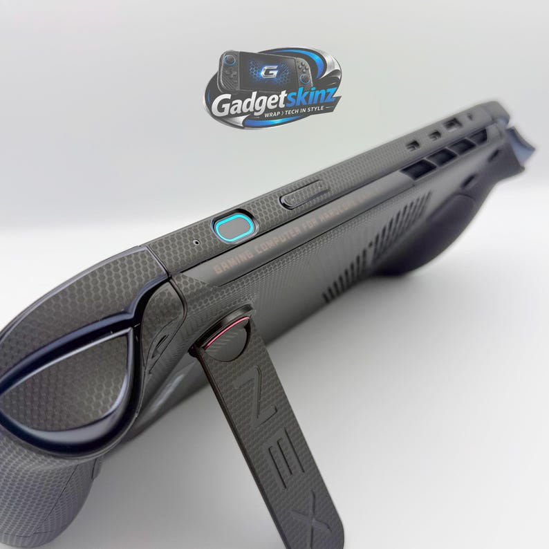 May include: A handheld gaming computer featuring a dark grey textured skin with a hexagonal pattern. The device includes a built-in kickstand with the letter Z embossed on it, a power button with a blue light ring, and various ports along the top edge.