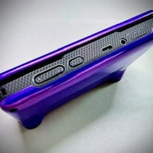 May include: A glossy purple phone case with a built-in stand. The case has a textured, dark gray interior and features buttons and ports along the side. The stand is integrated into the bottom of the case.