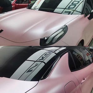 May include: A two-part image showcasing a pink car with a black roof. The car's body has a matte finish. The top image shows the front of the car, while the bottom image shows the rear. The car is parked indoors.