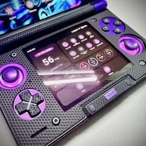 May include: A handheld gaming device with a dark gray carbon fiber texture and purple accents. The device features a screen displaying a user interface with various icons and data. It has purple control buttons and joysticks, and a stylus.