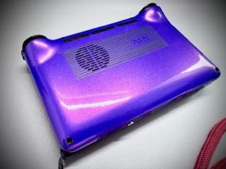 May include: A glossy, purple electronic device with a vent and speaker. The device has rounded corners and a textured surface. The word "AVN" is visible on the top. The device is on a white surface.