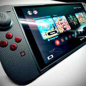 Könnte beinhalten: Eine schwarze und graue Nintendo Switch-Konsole mit strukturierter Grifffläche und roten Knöpfen. Der Bildschirm zeigt Spielsymbole, darunter "The Legend of Zelda" und "Diablo". Die Konsole ist abgewinkelt und zeigt den Bildschirm und den Controller.