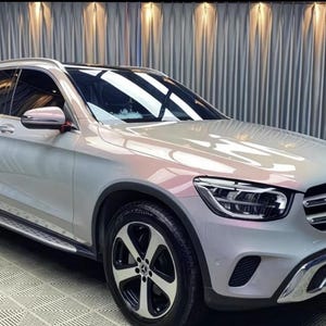 May include: A silver SUV with black wheels and a black roof. The vehicle has a chrome grill and side mirrors. The car is parked in front of a silver curtain.