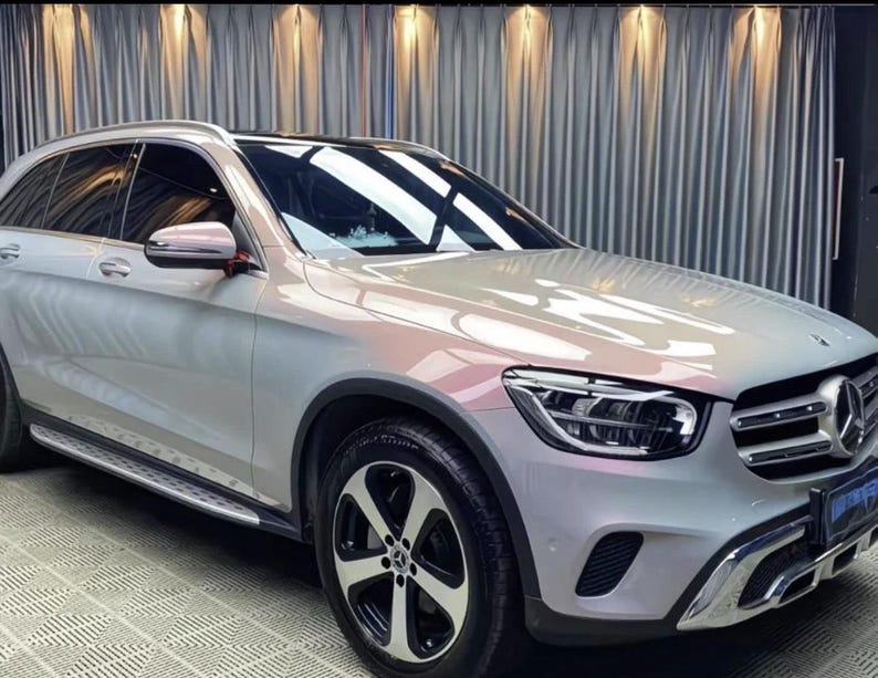May include: A silver SUV with black wheels and a black roof. The vehicle has a chrome grill and side mirrors. The car is parked in front of a silver curtain.