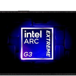 May include: A handheld gaming console with a dark grey hexagonal pattern on the outer casing, featuring black joysticks with teal rings, a directional pad, and action buttons. The screen displays a blue Intel Arc Extreme G3 logo graphic.