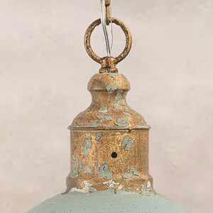 May include: Close-up of a vintage-style pendant light fixture. The fixture features a distressed gold finish with teal accents. A circular ring and chain are attached to the top for hanging. The light has a bell-shaped shade.