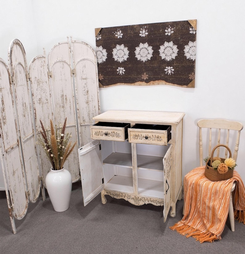 May include: White wooden cabinet with two drawers and two doors. The cabinet has a distressed finish and carved floral details. The cabinet is open, revealing shelves inside.