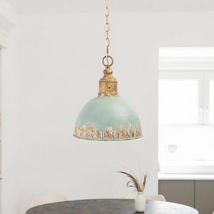 May include: A vintage-style pendant light with a distressed, light blue dome shade and a gold-colored top. The light hangs from a chain. The fixture is suspended above a dark gray table. The overall aesthetic is rustic and industrial.