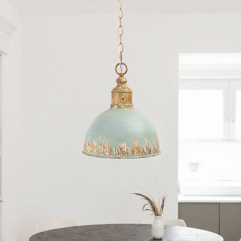 May include: A vintage-style pendant light with a distressed, light blue dome shade and a gold-colored top. The light hangs from a chain. The fixture is suspended above a dark gray table. The overall aesthetic is rustic and industrial.