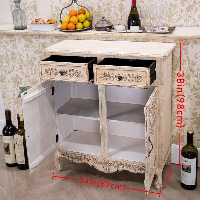 May include: White distressed wood cabinet with two drawers and two doors. The cabinet has carved details and measures 38 inches tall and 34 inches wide.