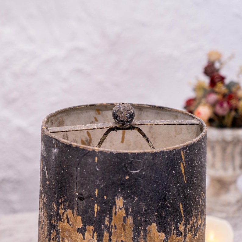 May include: A black and gold lampshade with a metal frame and a round knob on top. The lampshade has a distressed finish, giving it a vintage look.