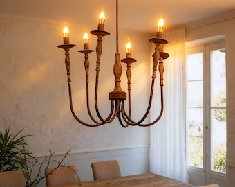 May include: A rustic, eight-light chandelier with a distressed brown finish. The fixture features curved arms and candle-style lights, suspended above a wooden dining table. The room has a neutral color palette with a window and sheer curtains.