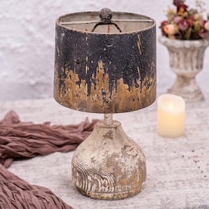 May include: A distressed wooden table lamp with a black and gold lampshade. The lampshade has a distressed finish and the base is made of wood with a white paint finish.