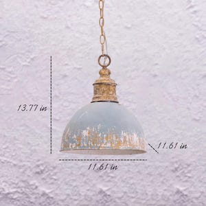 May include: A distressed, light blue pendant light with a gold-colored top and chain. The shade is 11.61 inches in diameter and 13.77 inches high. The light fixture has a vintage, rustic aesthetic.