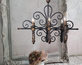 May include: Ornate black and gold chandelier with four lights. The fixture features scrolled ironwork and decorative candle holders. A small bouquet of pink and white flowers sits in a white vase below the chandelier.