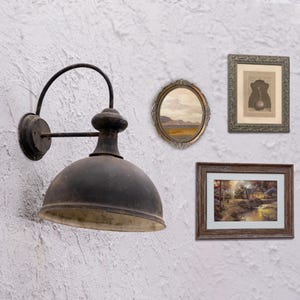 May include: A black metal wall sconce with a round, dome-shaped shade. The sconce is mounted on a white wall with three framed pictures, including a landscape scene and a framed print.