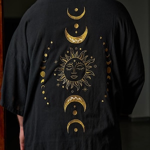 May include: Black kimono with gold embroidery of a sun and moon phases. The sun has a face and the moon phases are in a vertical line.
