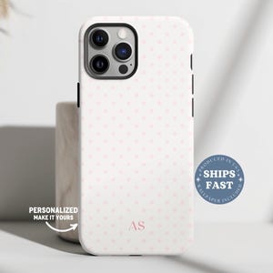 May include: White phone case with a pink polka dot pattern. The case has a black camera frame and black side buttons. The initials "AS" are in pink at the bottom. Text on the case says "Personalized Make It Yours" and "Ships Fast".