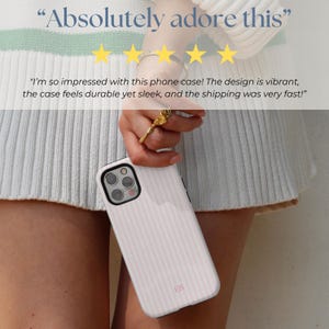 May include: A white phone case with pink stripes and a small "ER" logo. The case is being held by a person's hand. The text "Absolutely adore this" and five stars are visible above the case. The text "I'm so impressed with this phone case! The design is vibrant, the case feels durable yet sleek, and the shipping was very fast!" is visible below the case.