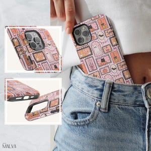 Puede incluir: Una funda de tel&eacute;fono de color rosa claro con un patr&oacute;n repetitivo de ilustraciones estilo sello postal que incluyen fantasmas, gatos negros, calabazas, murci&eacute;lagos, escobas y velas. La funda tiene un recorte negro para la c&aacute;mara y se muestra desde varios &aacute;ngulos.