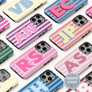 May include: A collection of smartphone cases featuring various striped patterns in multiple color combinations. Each case displays two large, bold, capitalized letters in a contrasting color. The cases have a triple-lens camera cutout.