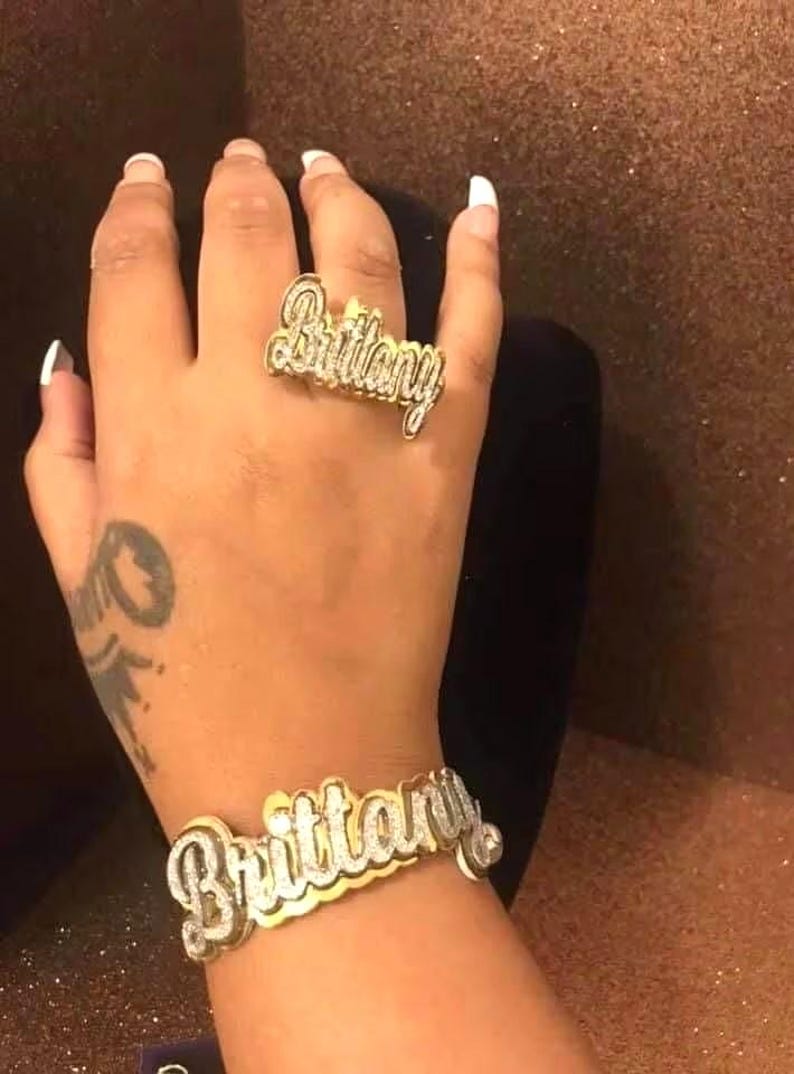Puede incluir: Un anillo y una pulsera de oro con el nombre "Brittany" escrito en brillantes diamantes de imitaci&oacute;n.