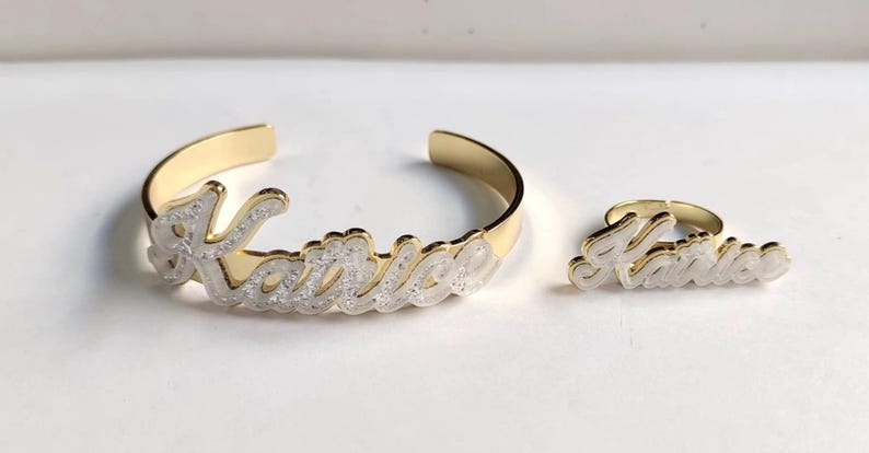 Puede incluir: Conjunto de pulsera y anillo de oro con el nombre "Katrice" escrito en purpurina blanca.