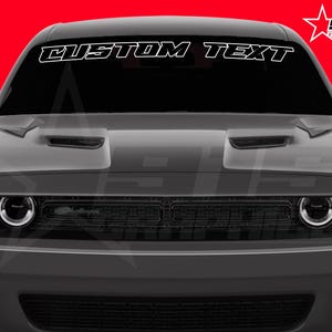 Puede incluir: Un coche gris con el texto "CUSTOM TEXT" en blanco en el parabrisas. El coche tiene una parrilla y faros negros. El fondo es rojo y un logotipo de estrella blanca está en la esquina superior derecha.