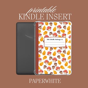 Puede incluir: Inserción imprimible para Kindle Paperwhite con un fondo blanco y un patrón de setas rojas, bellotas marrones y hojas amarillas. El texto "this kindle belongs to" está en un cuadro blanco.