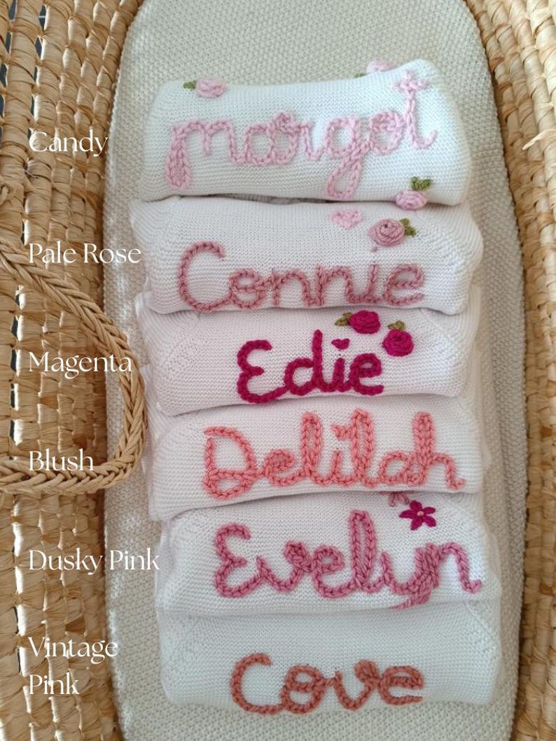 May include: A stack of white baby blankets embroidered with names in various shades of pink. The names include Margot, Connie, Edie, Delilah, Evelyn, and Cove. Each blanket has a different shade of pink embroidery.