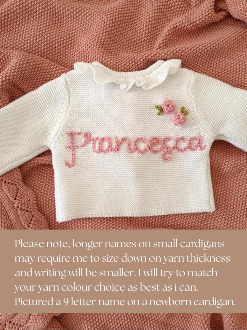 May include: White baby sweater with the name "Francesca" embroidered in pink. The sweater has a ruffled collar and two small pink rose appliqu&eacute;s. The sweater is displayed on a pink knitted blanket.
