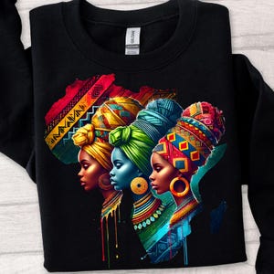 May include: Black sweatshirt with a colourful graphic of three women in profile, wearing patterned head wraps and jewellery. The design includes an outline of the African continent and detailed patterns.