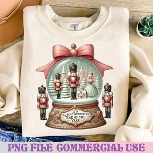 May include: Cream-colored sweatshirt featuring a snow globe design with nutcrackers, a princess, and winter scenery. The snow globe is topped with a pink bow. The text "IT'S THE MOST WONDERFUL TIME OF THE YEAR" is displayed on the base.
