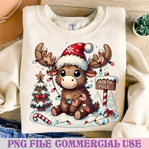 May include: Cream-colored sweatshirt featuring a cartoon moose wearing a Santa hat and Christmas lights. A Christmas tree, candy cane, and a "North Pole" sign are also depicted. The text "PNG FILE COMMERCIAL USE" is at the bottom.