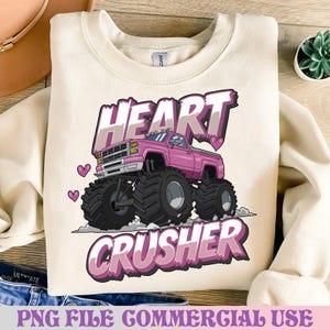 Könnte beinhalten: Cremefarbenes Sweatshirt mit einem rosa Monster-Truck-Motiv und den Worten "HEART CRUSHER". Der Truck hat große schwarze Reifen und Herzen. Der Satz "PNG FILE COMMERCIAL USE" steht unten. Das Sweatshirt ist gefaltet.