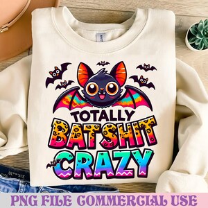 Puede incluir: Sudadera crema con un diseño de murciélago de dibujos animados con ojos grandes y alas coloridas. El texto "TOTALLY BAT SHIT CRAZY" está impreso en una fuente lúdica. Ilustraciones de murciélagos adicionales están dispersas. La frase "PNG FILE COMMERCIAL USE" está en la parte inferior.
