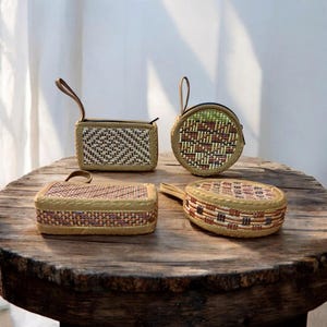 Könnte beinhalten: Vier gewebte Rattan-Taschen in verschiedenen Formen liegen auf einem Holztisch. Die Taschen umfassen eine rechteckige Box, eine runde Geldbörse und zwei weitere rechteckige und ovale Taschen, alle mit kleinen Griffen. Die Taschen haben braune, beige und tan Farben.