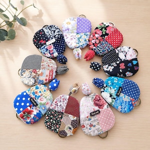 Puede incluir: Una colección de nueve bolsas de tela circulares dispuestas en círculo, cada una con un diseño de patchwork de varios patrones florales, de lunares y geométricos en colores que incluyen azul, rojo, rosa, morado y negro, con una pequeña flor de tela.