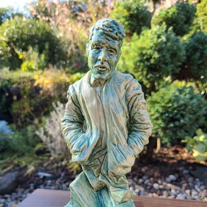 Puede incluir: Una escultura de cerámica de una persona con un esmalte verde. La escultura está de pie sobre una base de madera.
