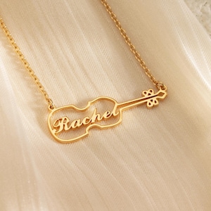 Può includere: Collana d'oro con un ciondolo a forma di violino con il nome "Rachel" ritagliato.