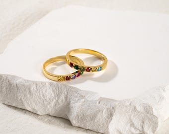 May include: Two gold rings with a row of colorful gemstones. The rings are stacked on top of each other.